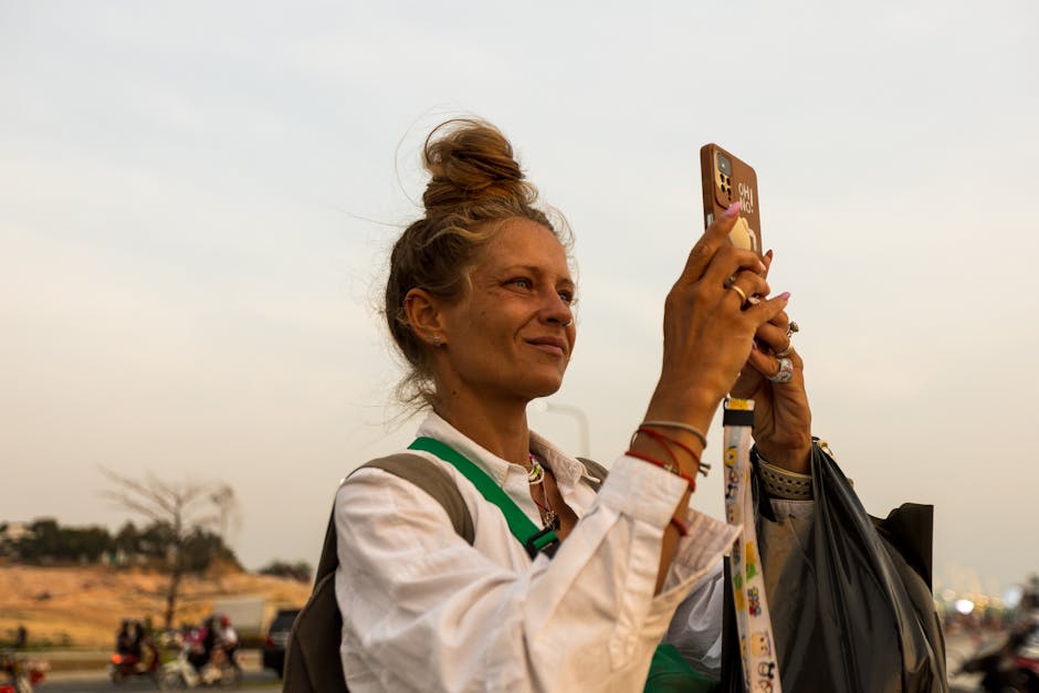 Young woman photographs a scenic view with smartphone at sunset, embodying travel and adventure.