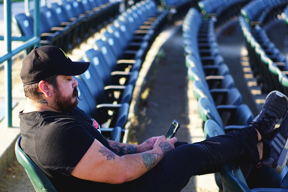Man with tattoos relaxing at stadium bleachers using a smartphone.