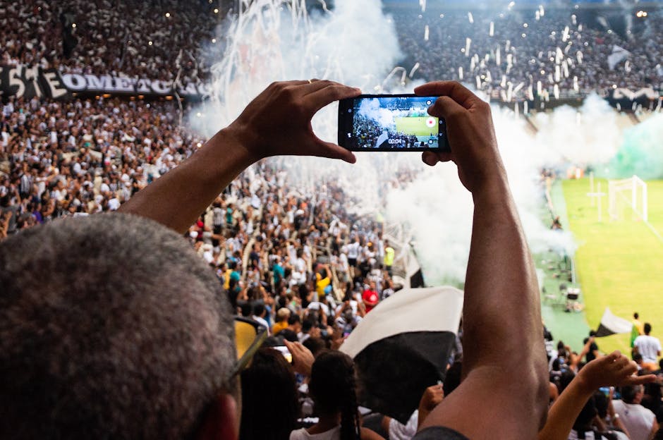 Thrilling football match scene with fans capturing the moment on a smartphone from the stadium stands.